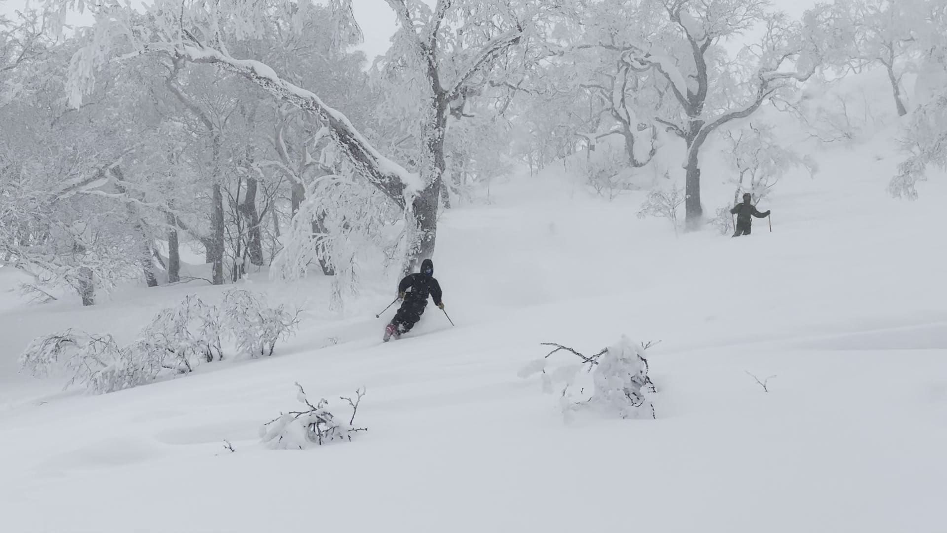 A skier resting in deep powder beneath a mountain ridge in Japan.